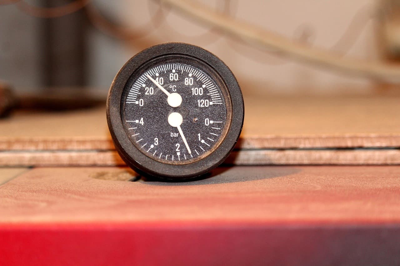 A round dial gauge with a black face and white needle resting on a ledge