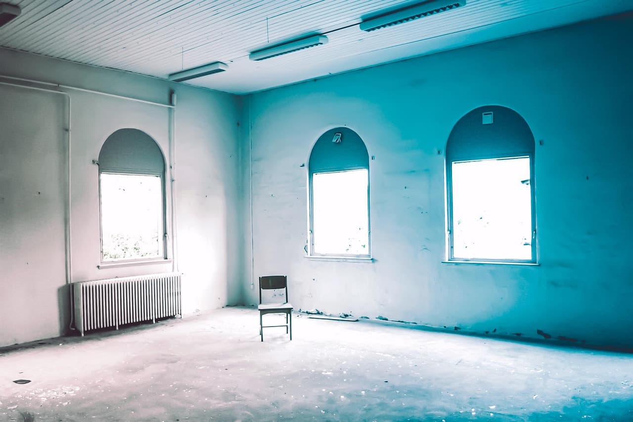 A cold, empty room with an old column radiator under tall arched windows