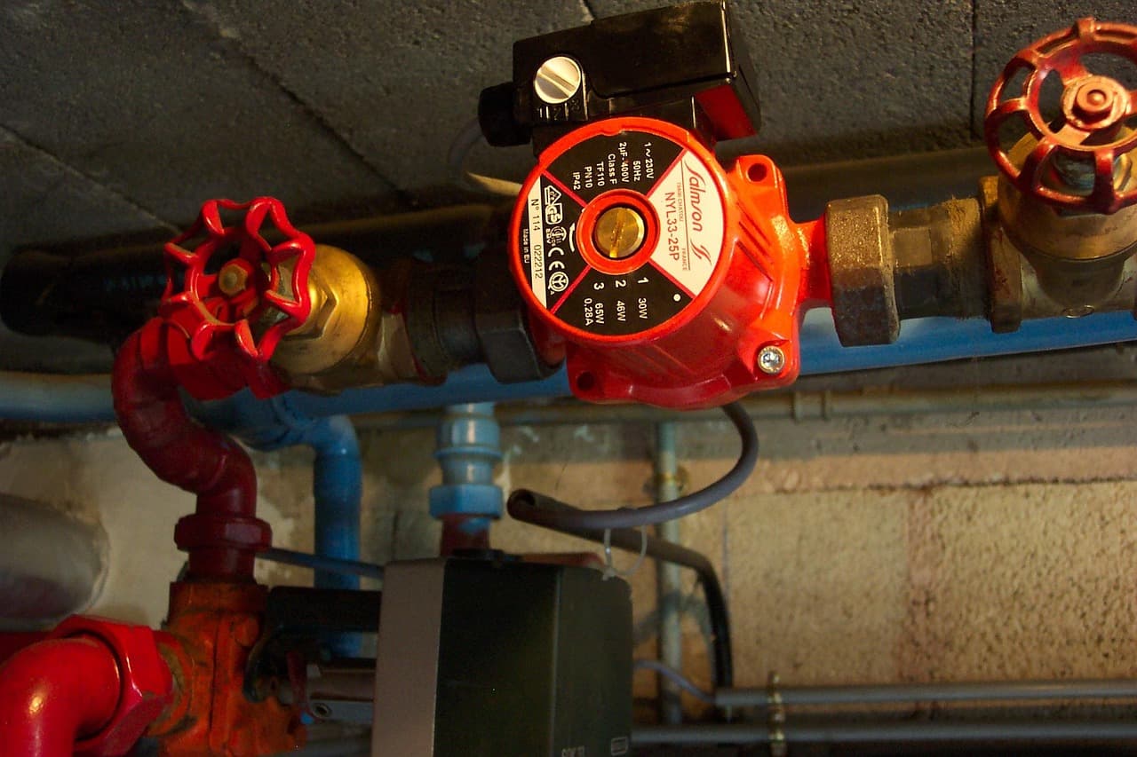 A red circulating pump and red-handled valves on the pipework under a boiler