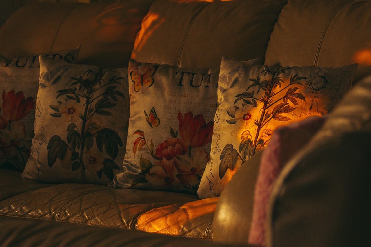 A sofa with floral cushions lit by warm lamplight in the evening